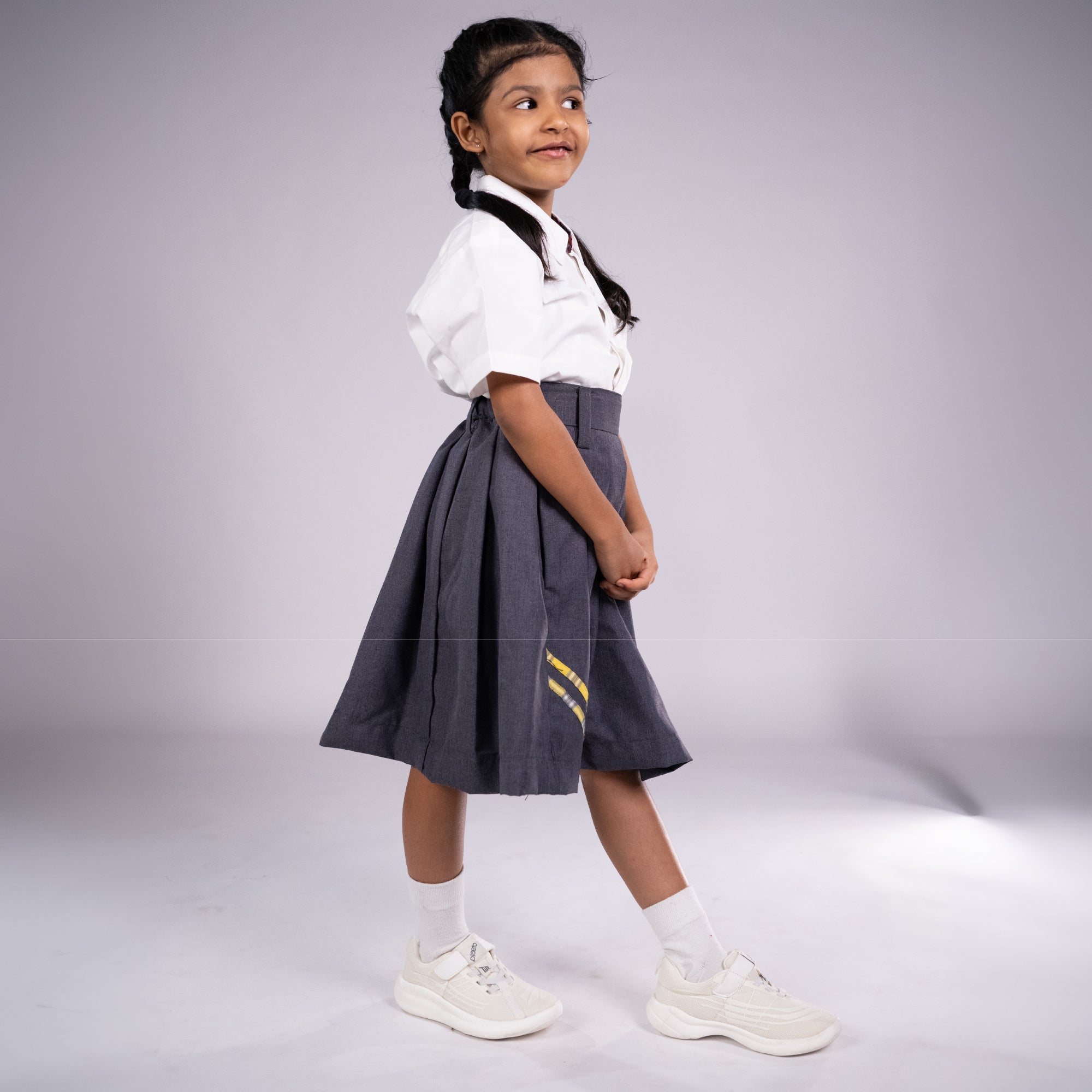 Young girl wearing a white shirt and gray skirt with a yellow detail on a plain background